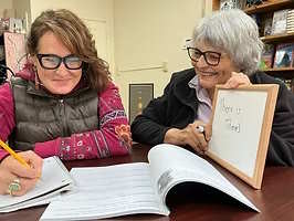 Two women during a tutoring session, one writing in a workbook, the other holding a whiteboard.