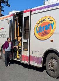 Senior Library Assistant and Bookmobile Driver, Katie, standing next to the Bookmobile.