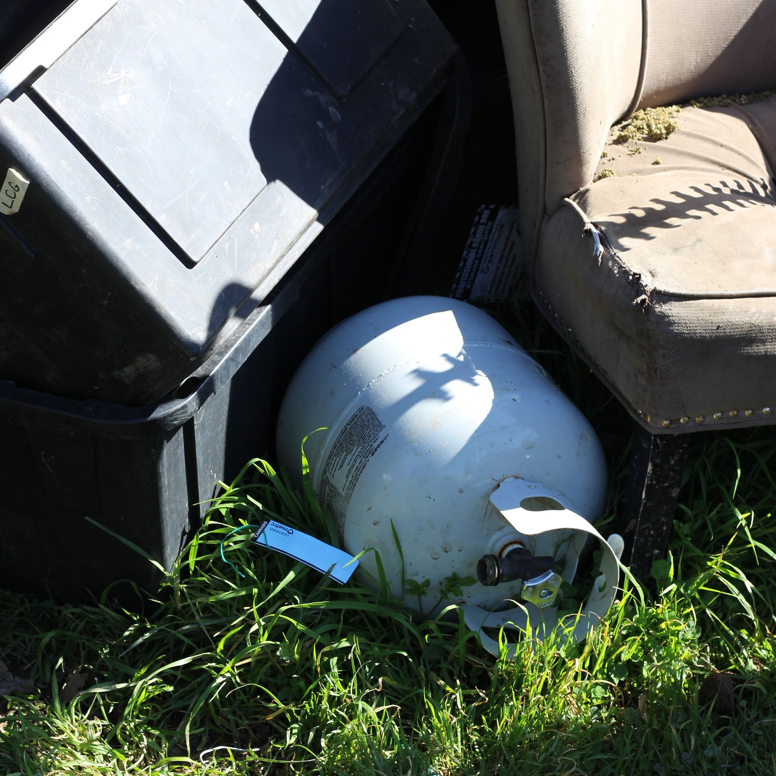 Black totes, blue state-license cannabis tag, propane tank, chair
